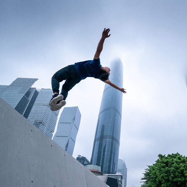 A skateboarder in the air in front of a skyscraper.