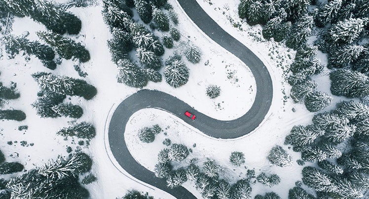 An aerial view of a car driving down a snowy road.
