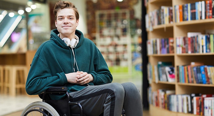 A young man in a wheelchair sitting in front of a book shelf.
