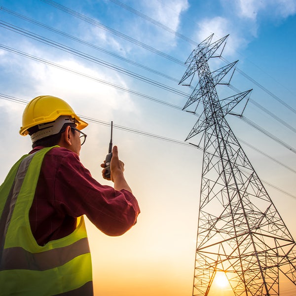 A man holding a radio in front of high voltage pylons.