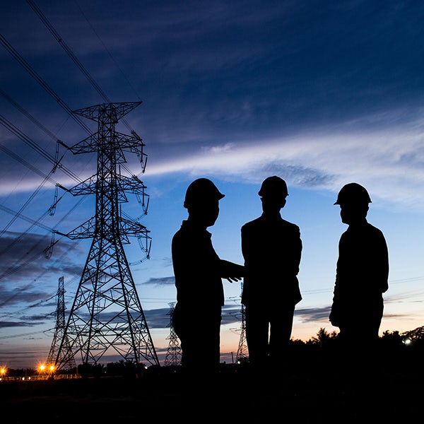 Silhouettes of three men standing in front of a power line at dusk.
