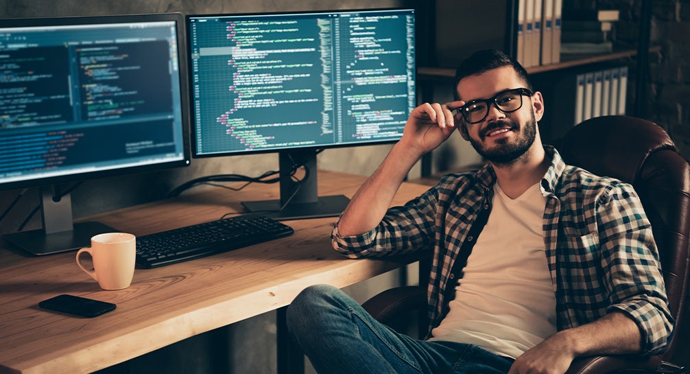 A man sitting in front of two monitors with code on them.