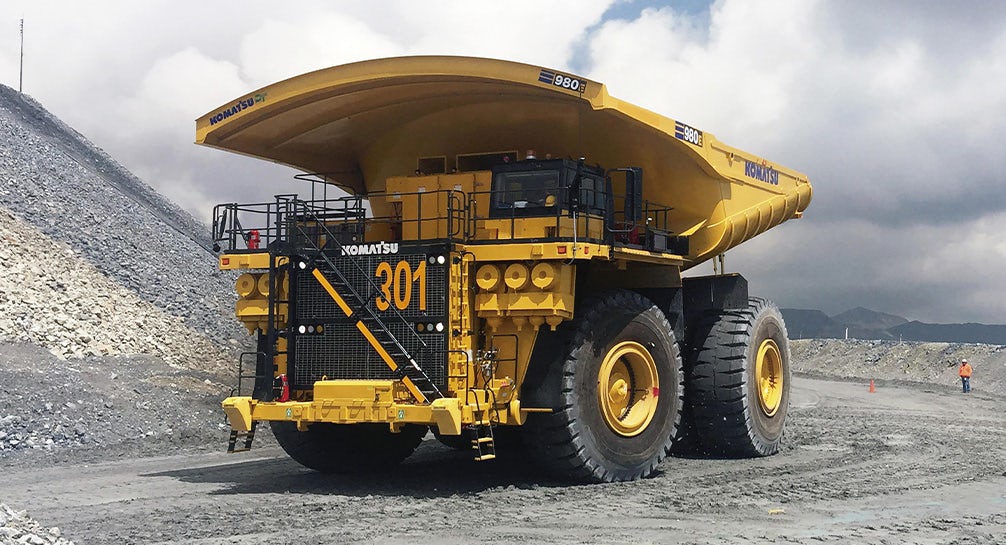 A large yellow dump truck is parked on a gravel road.