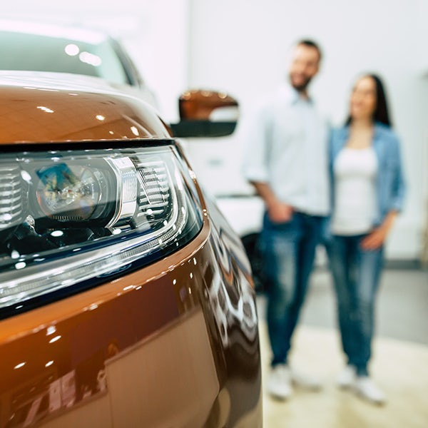 A man and woman standing next to a car in a showroom.
