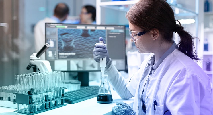 A woman in a lab coat is working on a computer.