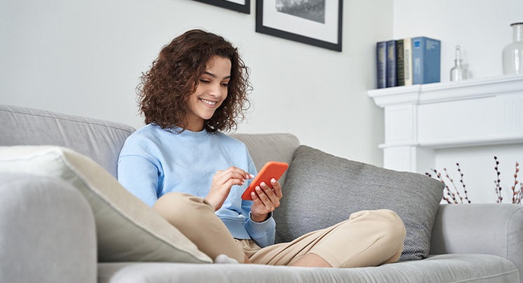 A young woman sitting on a couch and using a cell phone.
