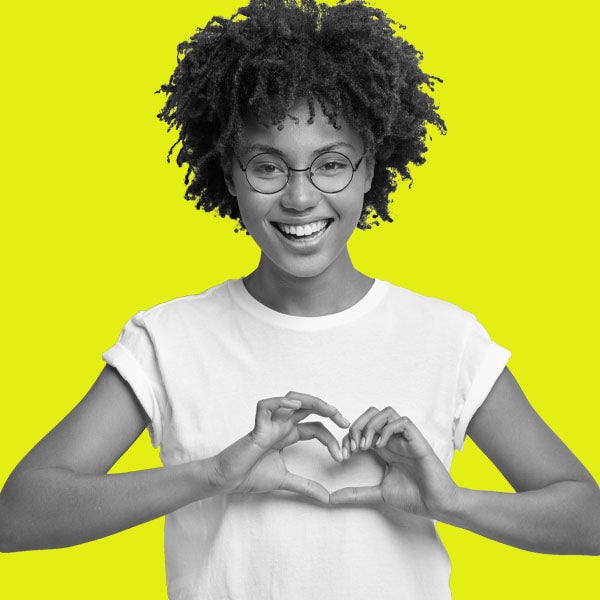 Young african american woman making a heart with her hands on a yellow background.