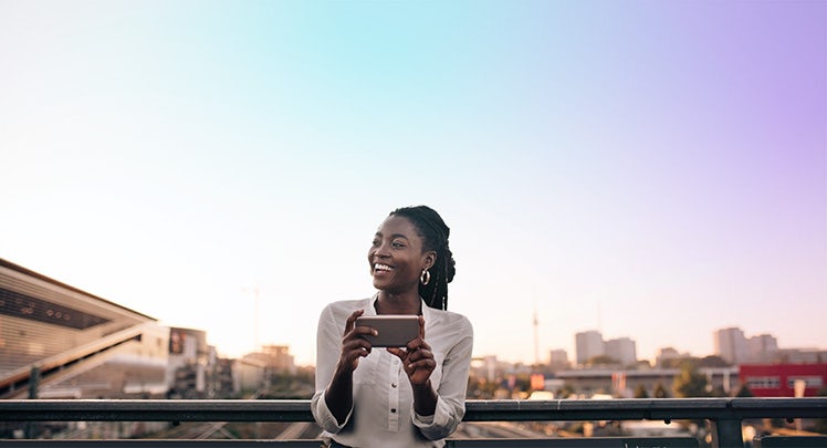 A young black woman holding a cell phone in a city.