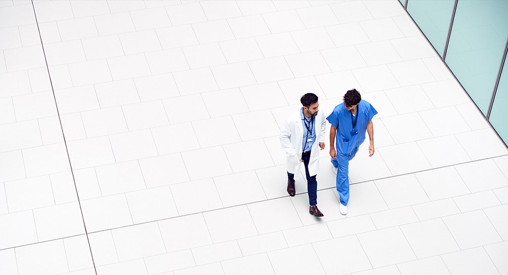 Two doctors walking on a white floor in a hospital.