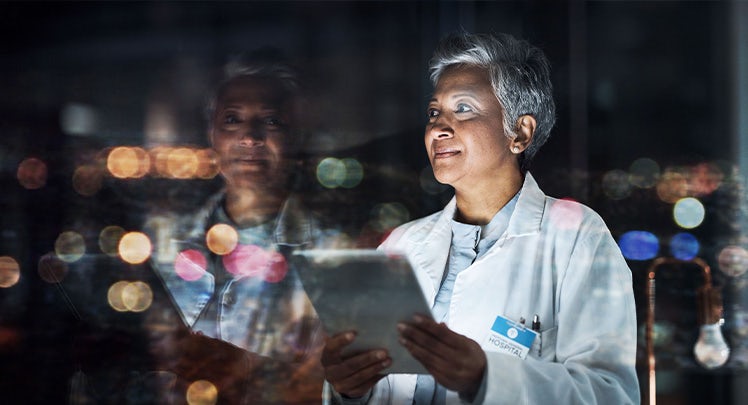 A woman in a lab coat looking at a tablet at night.
