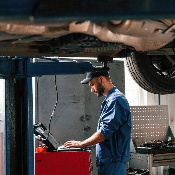 A mechanic working on a laptop under a car.