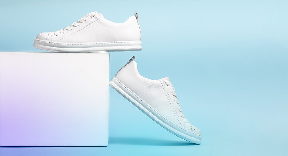 A pair of white sneakers on top of a box on a blue background.