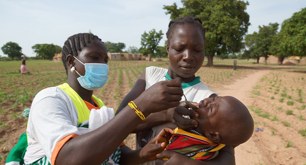 A woman is giving a child a vaccine in a field.