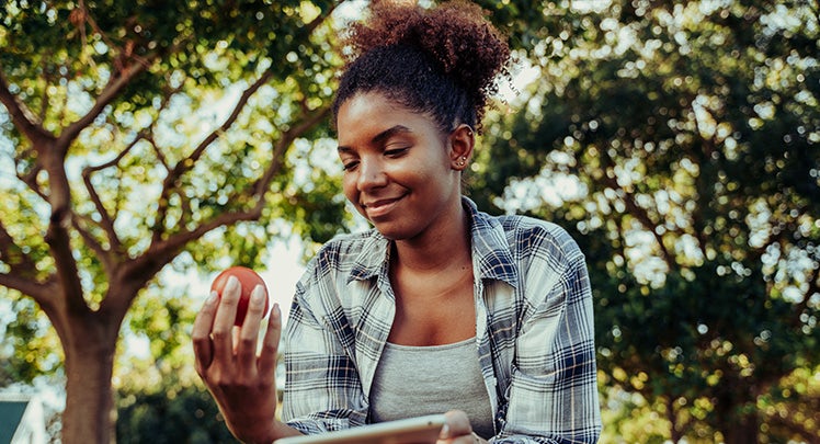 A young woman holding an apple in her hand while sitting in a park.