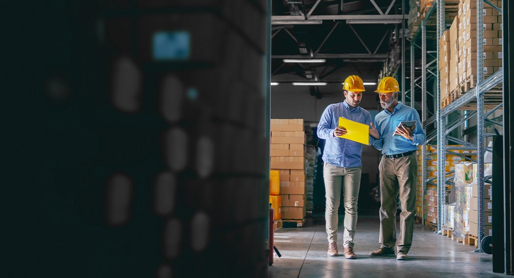 Two men in hard hats standing in a warehouse.