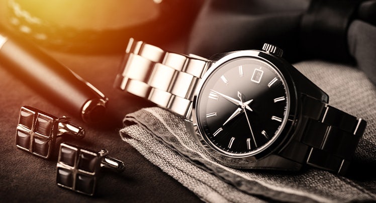 A watch, tie and cufflinks on a black background.