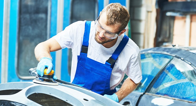 A man is sanding a car in a garage.