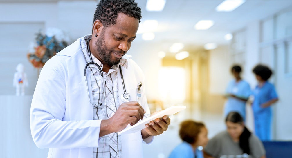 A male doctor writing on a tablet in a hospital.
