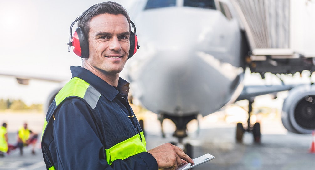 A man holding a tablet in front of an airplane.