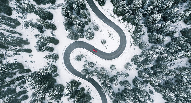 An aerial view of a car driving down a snowy road.