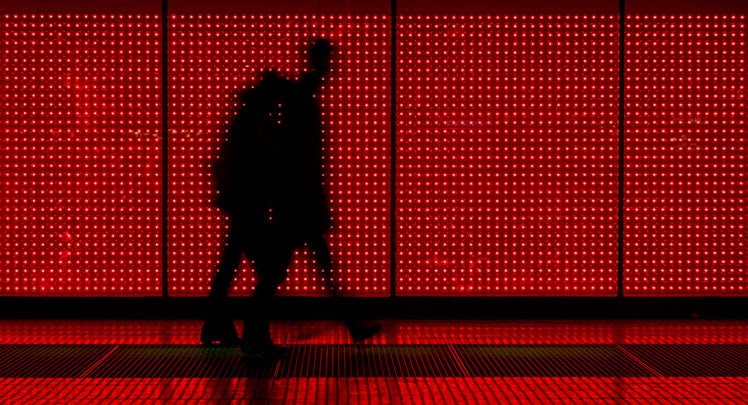 Two people walking in front of a red led wall.