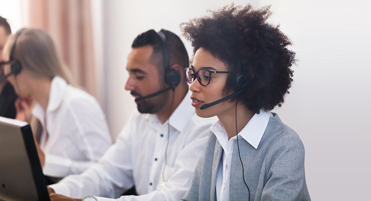 A group of people wearing headsets in a call center.