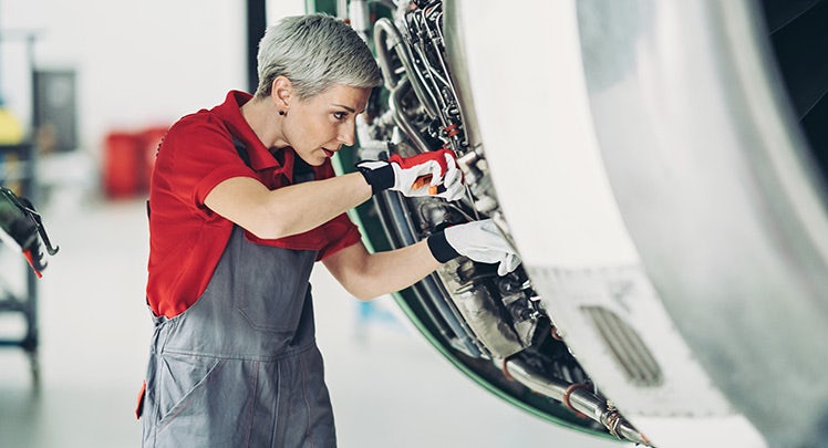 A woman in overalls is working on an airplane engine.