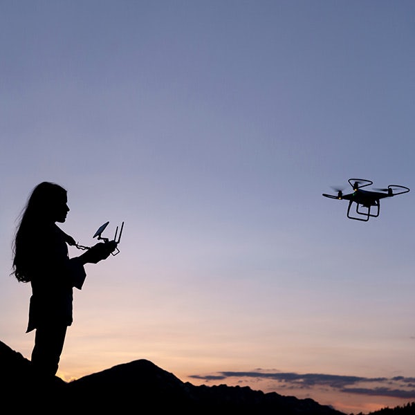 A woman is flying a drone at sunset.