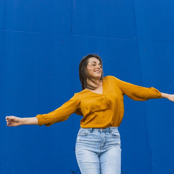 A woman in a yellow shirt is dancing in front of a blue wall.