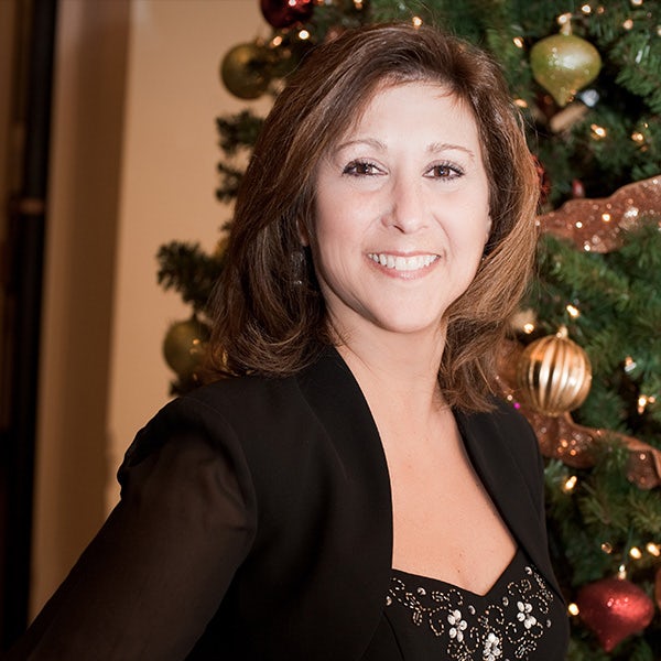 A woman smiling in front of a christmas tree.