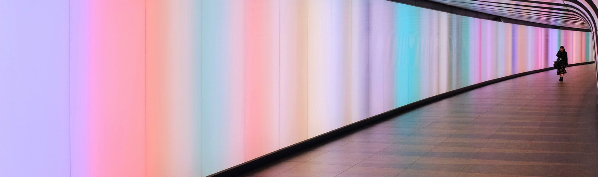 A person walking down a hallway with a rainbow colored wall.
