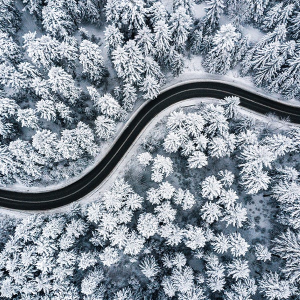 An aerial view of a winding road in a snowy forest.