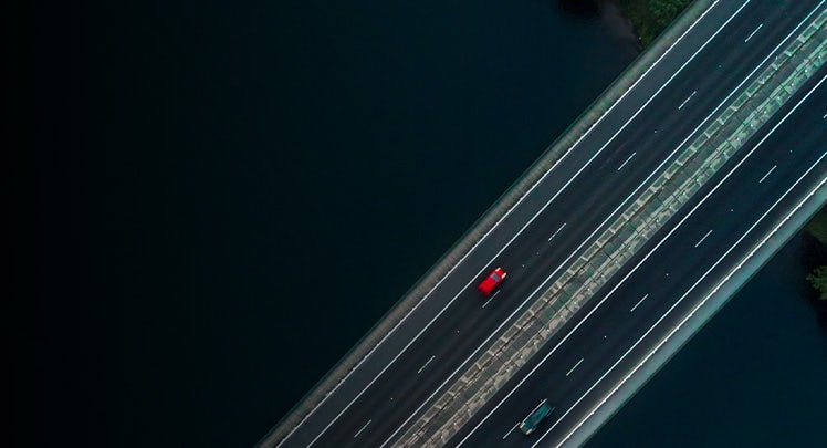 An aerial view of a red car driving on a bridge.