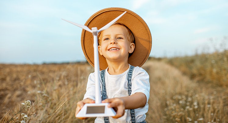 A young boy holding a wind turbine in a field.