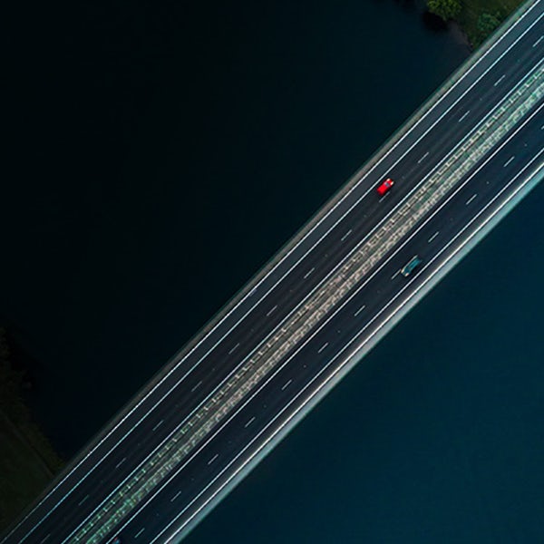 A red car driving on a bridge over a body of water.