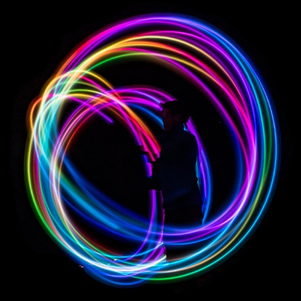 A person is holding a colorful hula hoop in front of a black background.