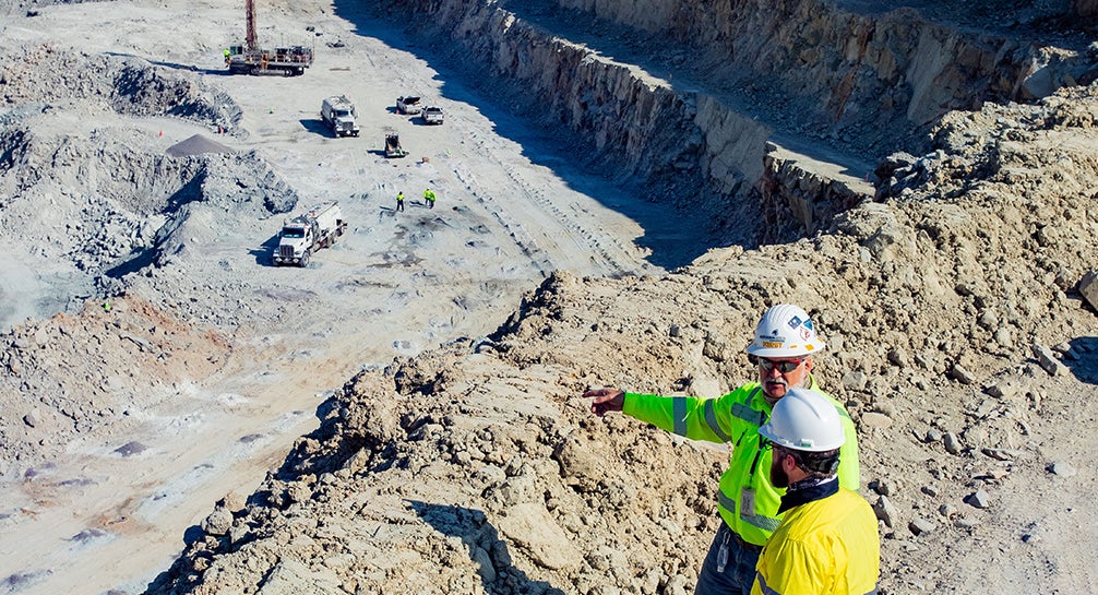 Two construction workers standing on top of a pile of dirt.