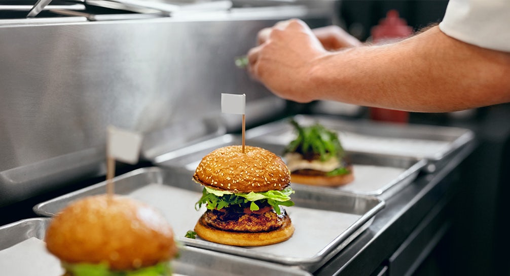 A chef is preparing burgers on trays in a kitchen.
