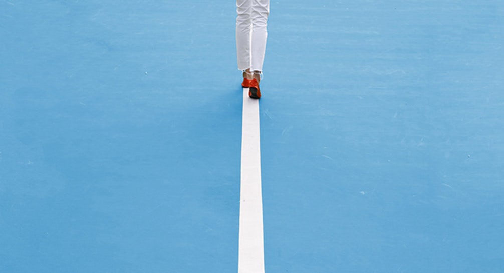 A woman with a tennis racket walking on a blue tennis court.