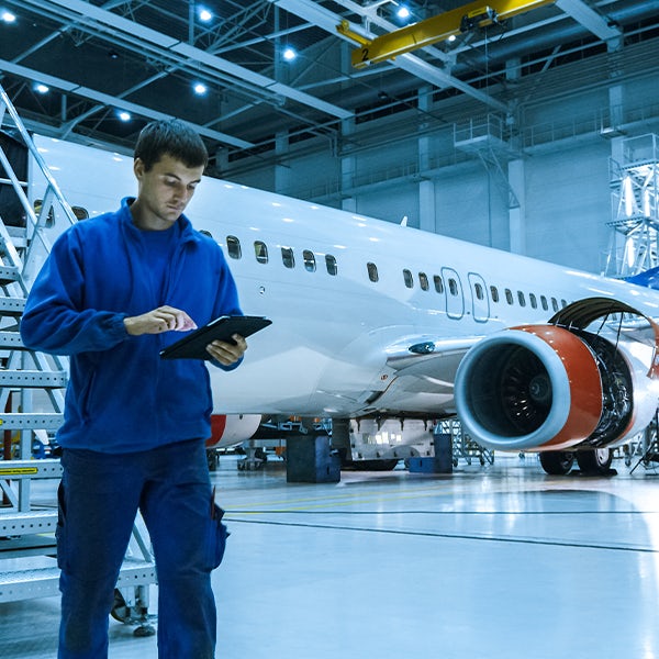 A man holding a tablet in front of an airplane.