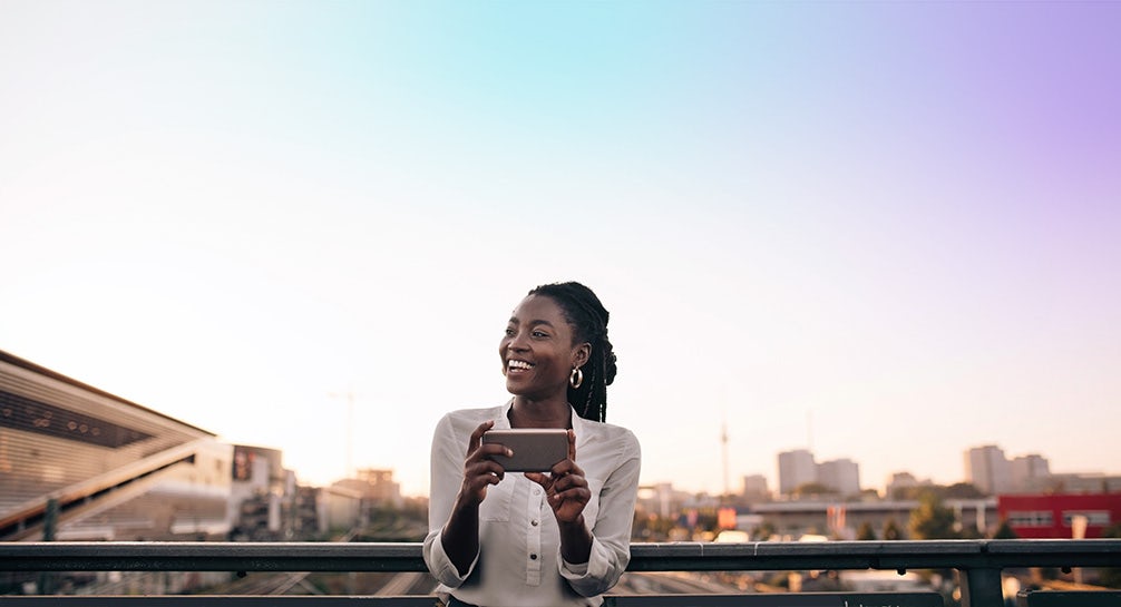 A black woman holding a cell phone while looking at the sky.