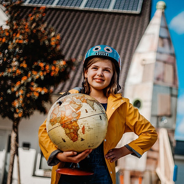 A girl holding a globe in front of a house.
