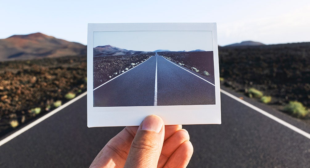 A person holding a polaroid photo of a desert road