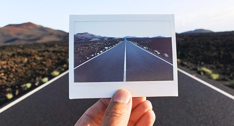 A person holding a polaroid photo of a desert road
