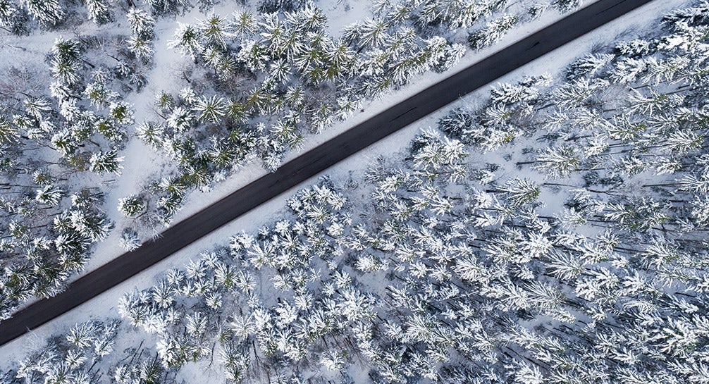 An aerial view of a snowy road in a forest.