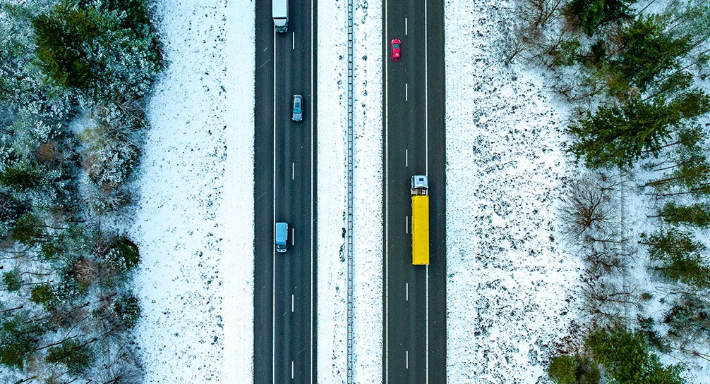 An aerial view of a snowy road with cars driving on it.