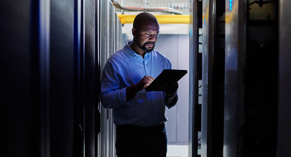 A man using a tablet in a server room.