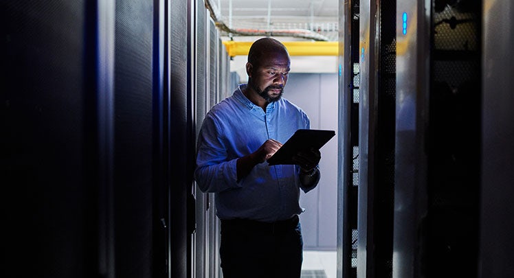 A man standing in a server room holding a tablet.