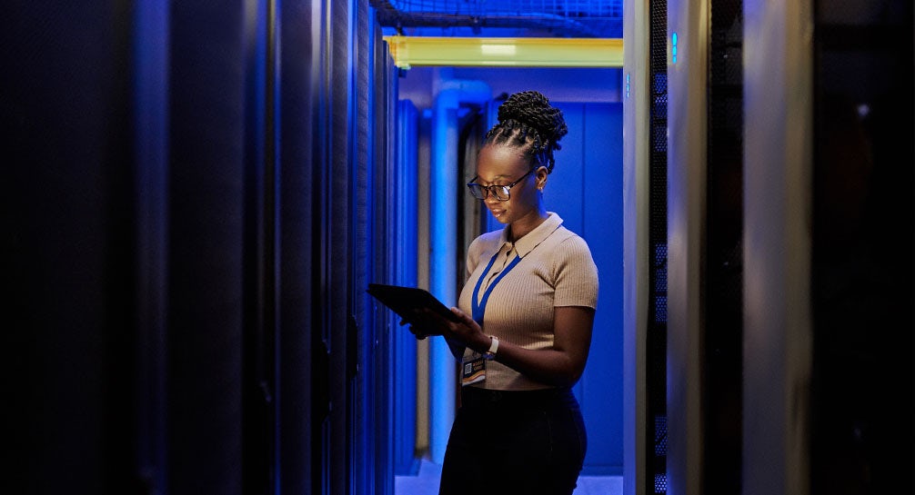 A woman using a tablet in a server room.