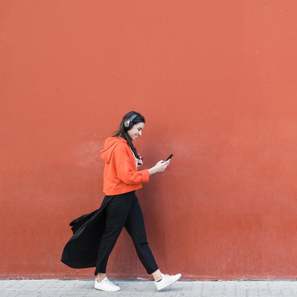 A woman is walking down the street while using her cell phone.